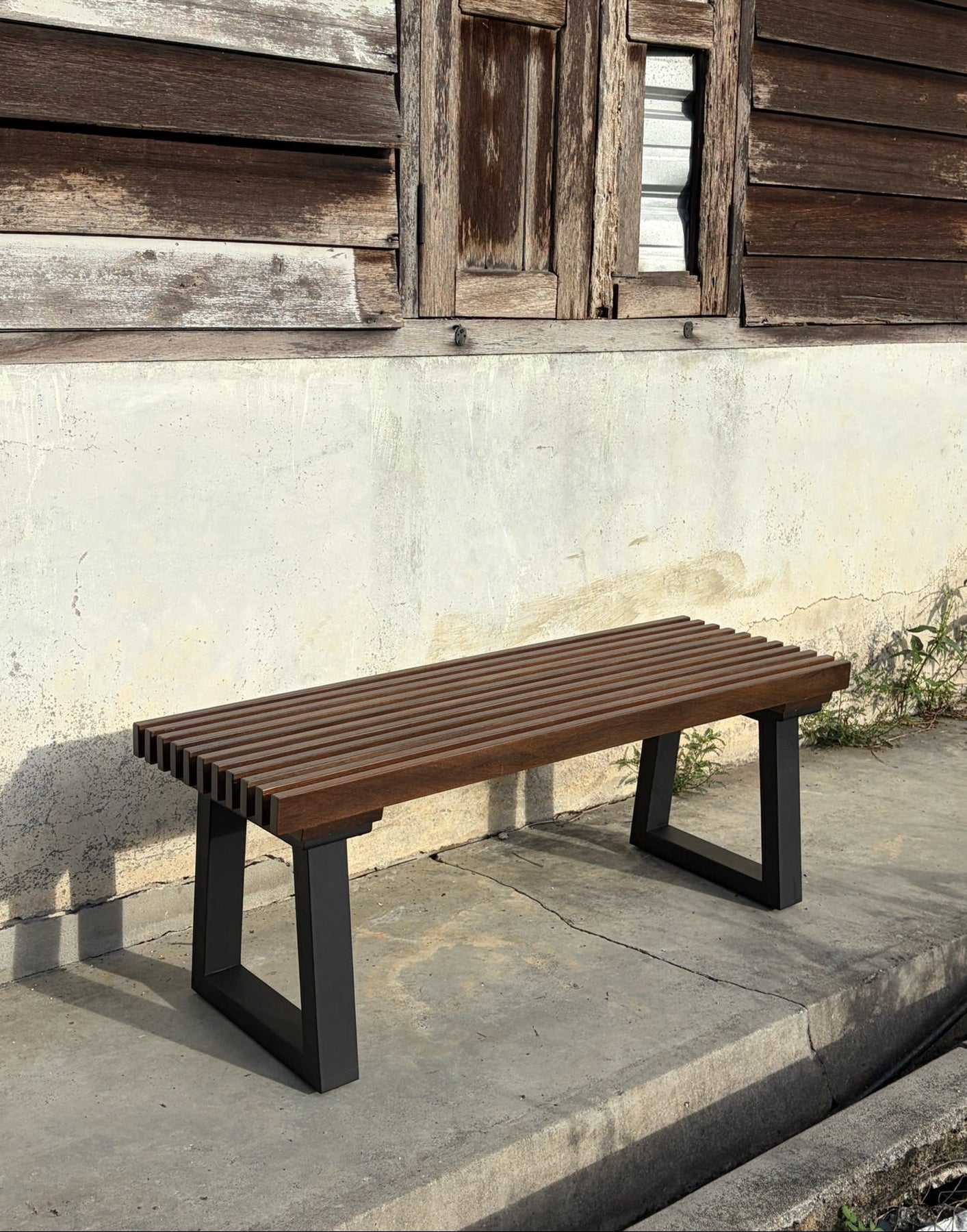 Wooden bench with black legs against a rustic wooden wall.