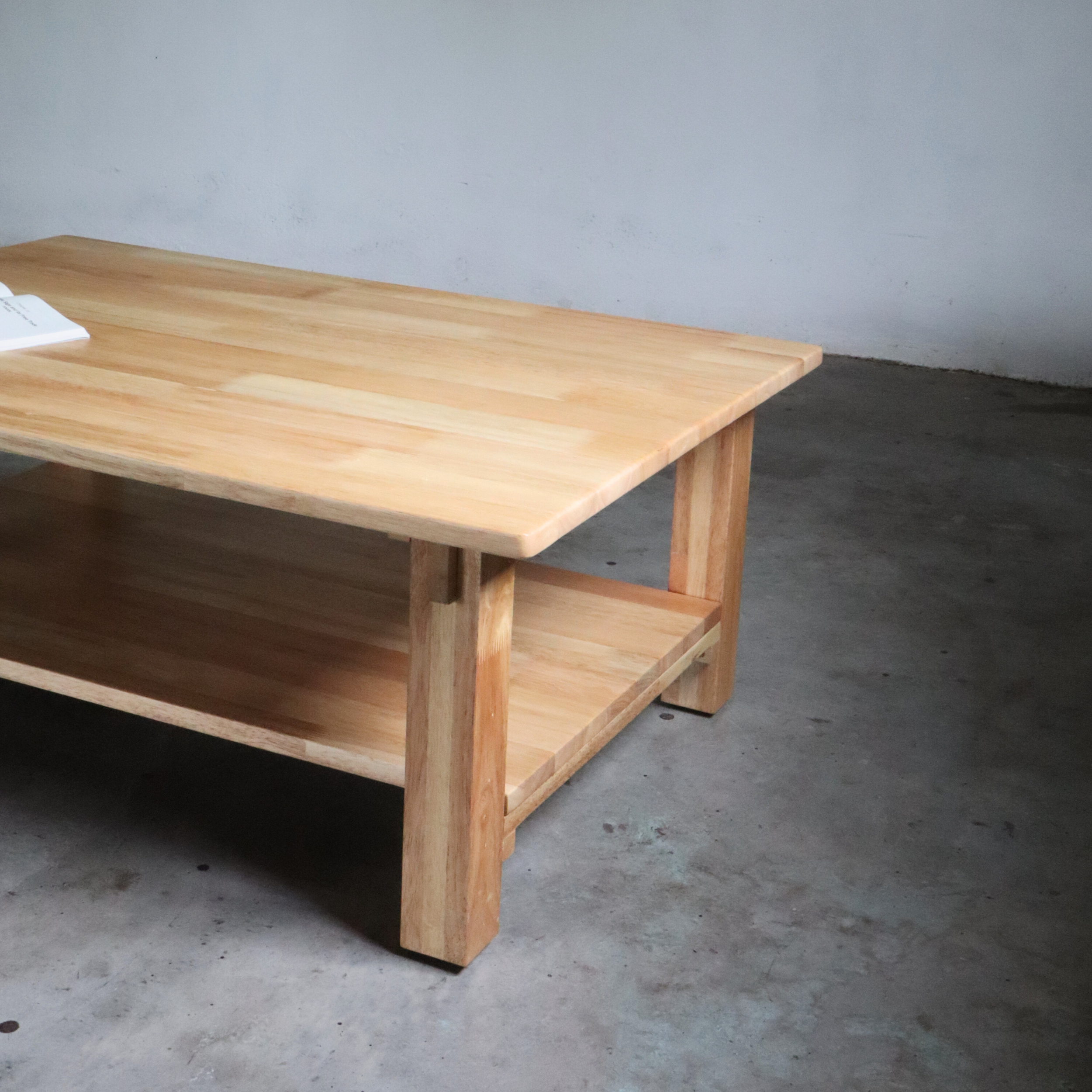 Wooden coffee table with a shelf on a concrete floor against a plain wall