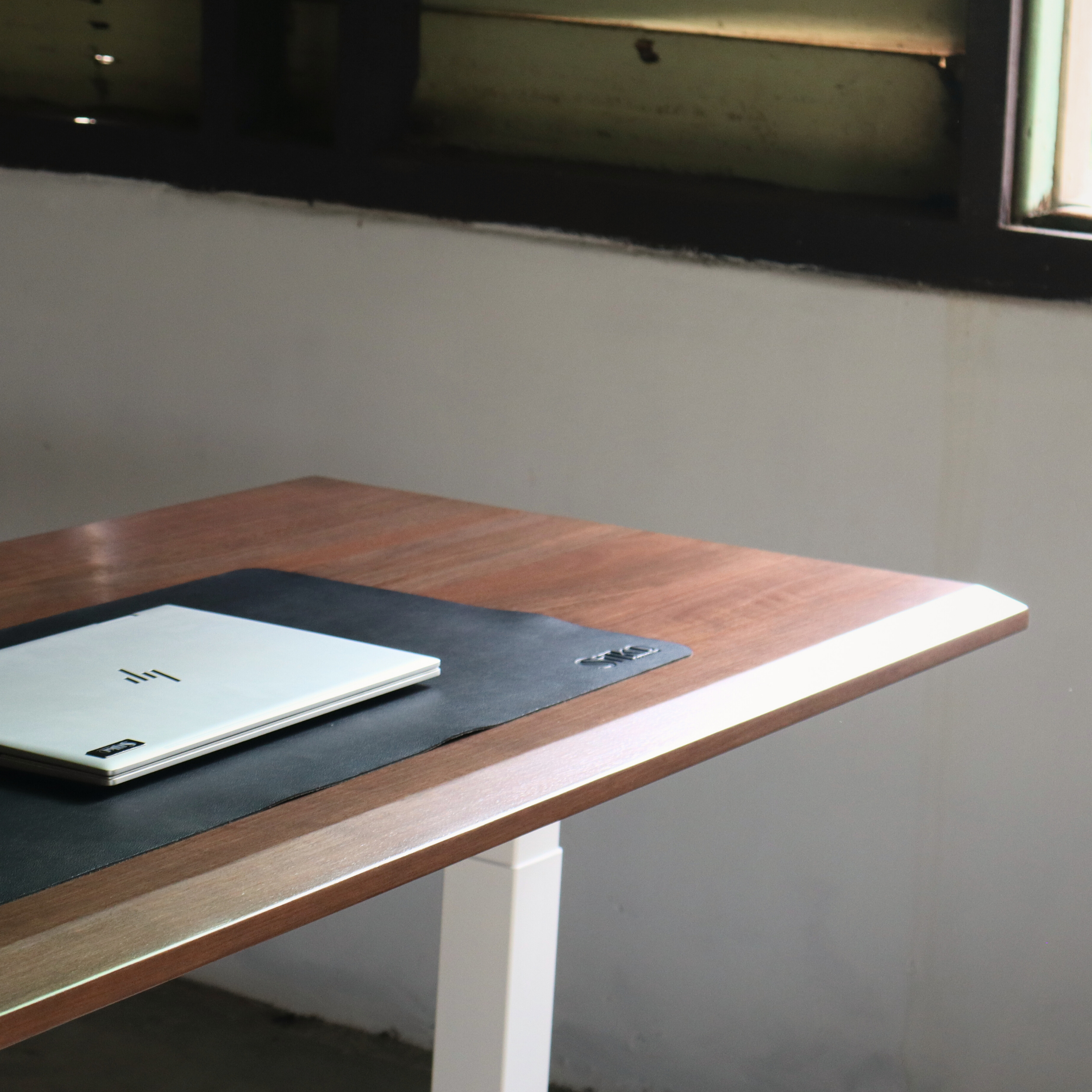 Wooden standing desk with a laptop on a black surface, against a plain wall.