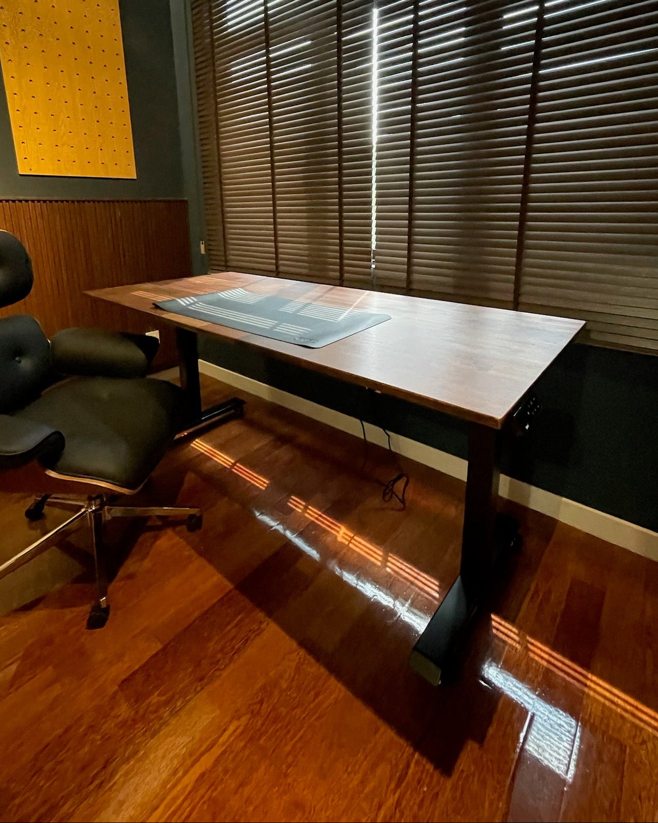 Home office with a desk and chair in a room with wooden flooring and a window with blinds.