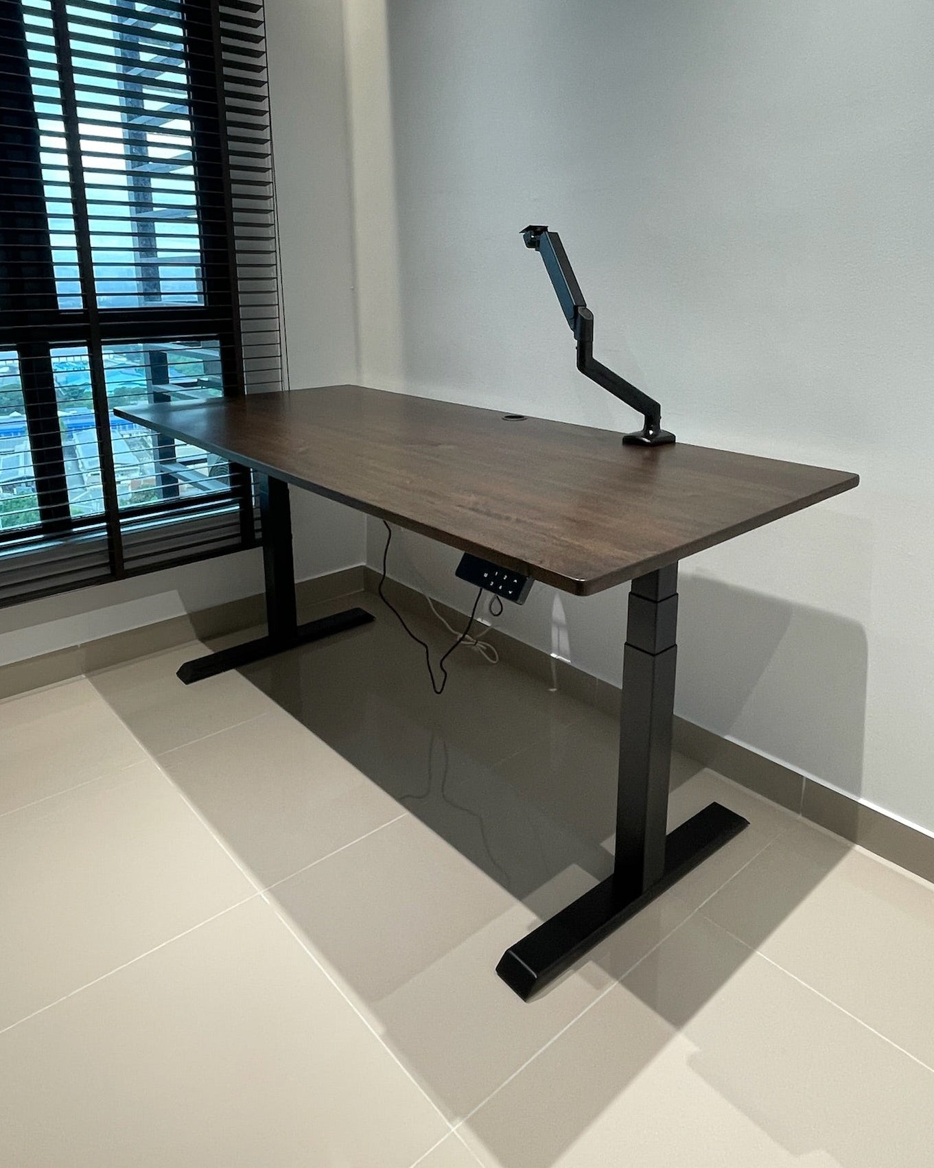 Wooden standing desk with adjustable monitor stand in a room with a window.