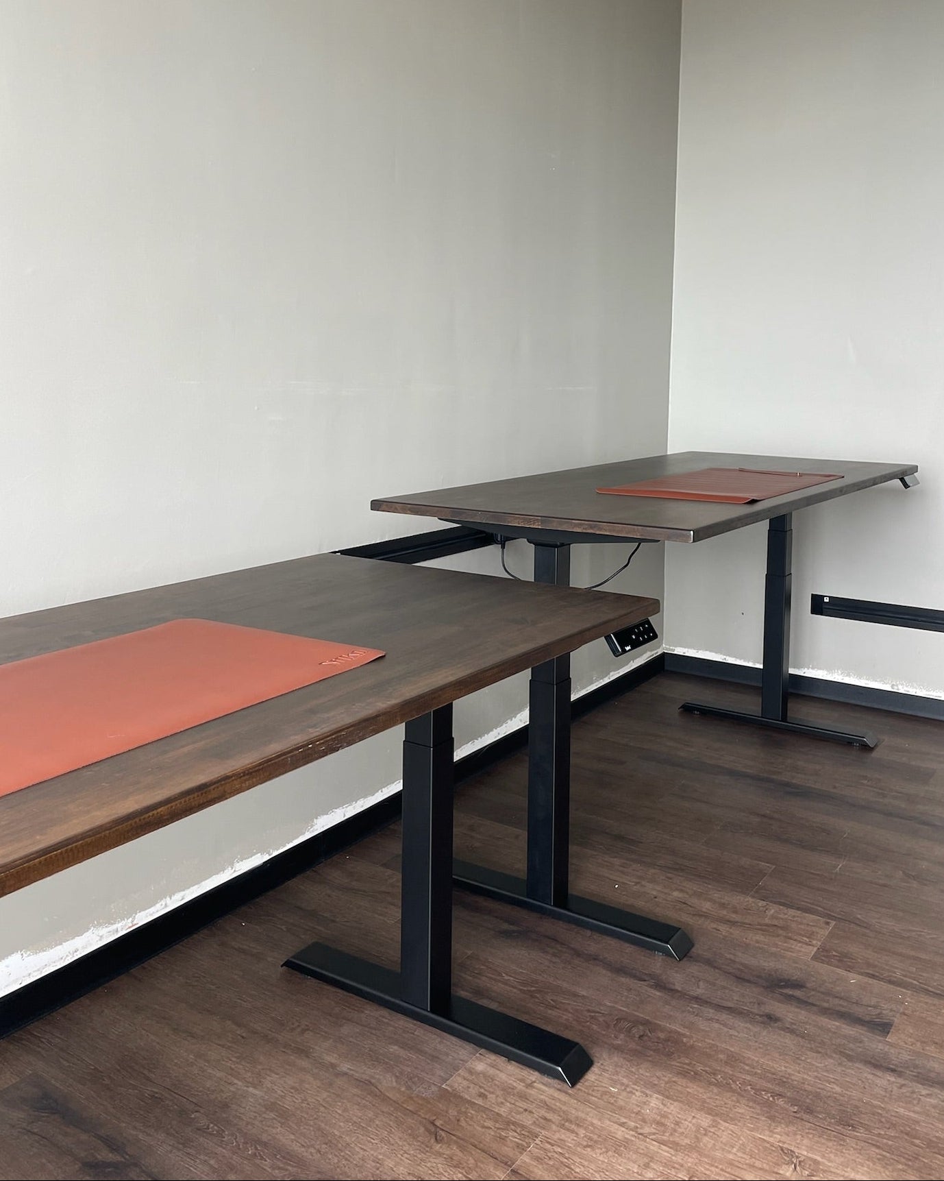 Two adjustable height desks with keyboard pad on a wooden floor.