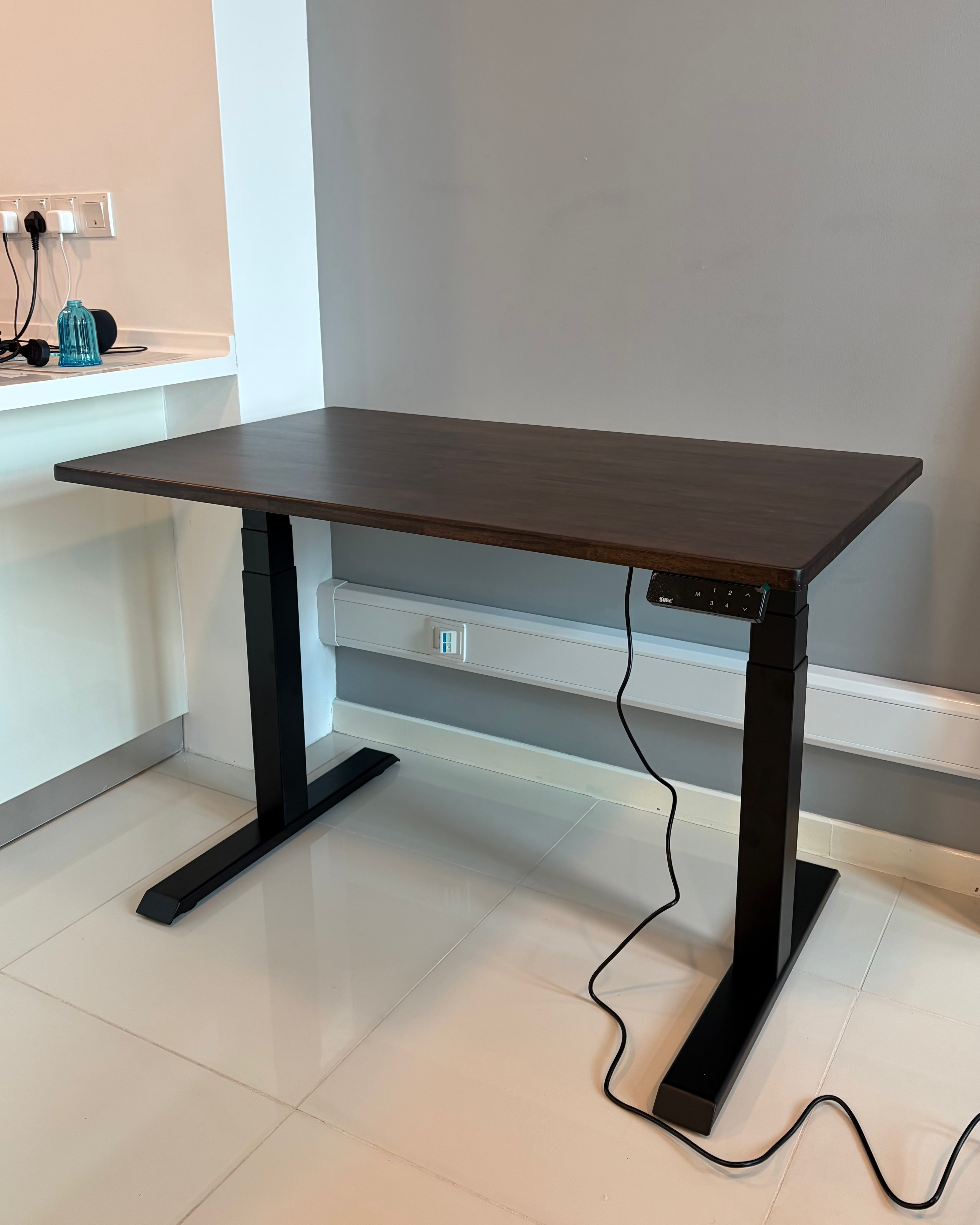 Dark wooden standing desk with black legs in a room with white walls and tiled floor.