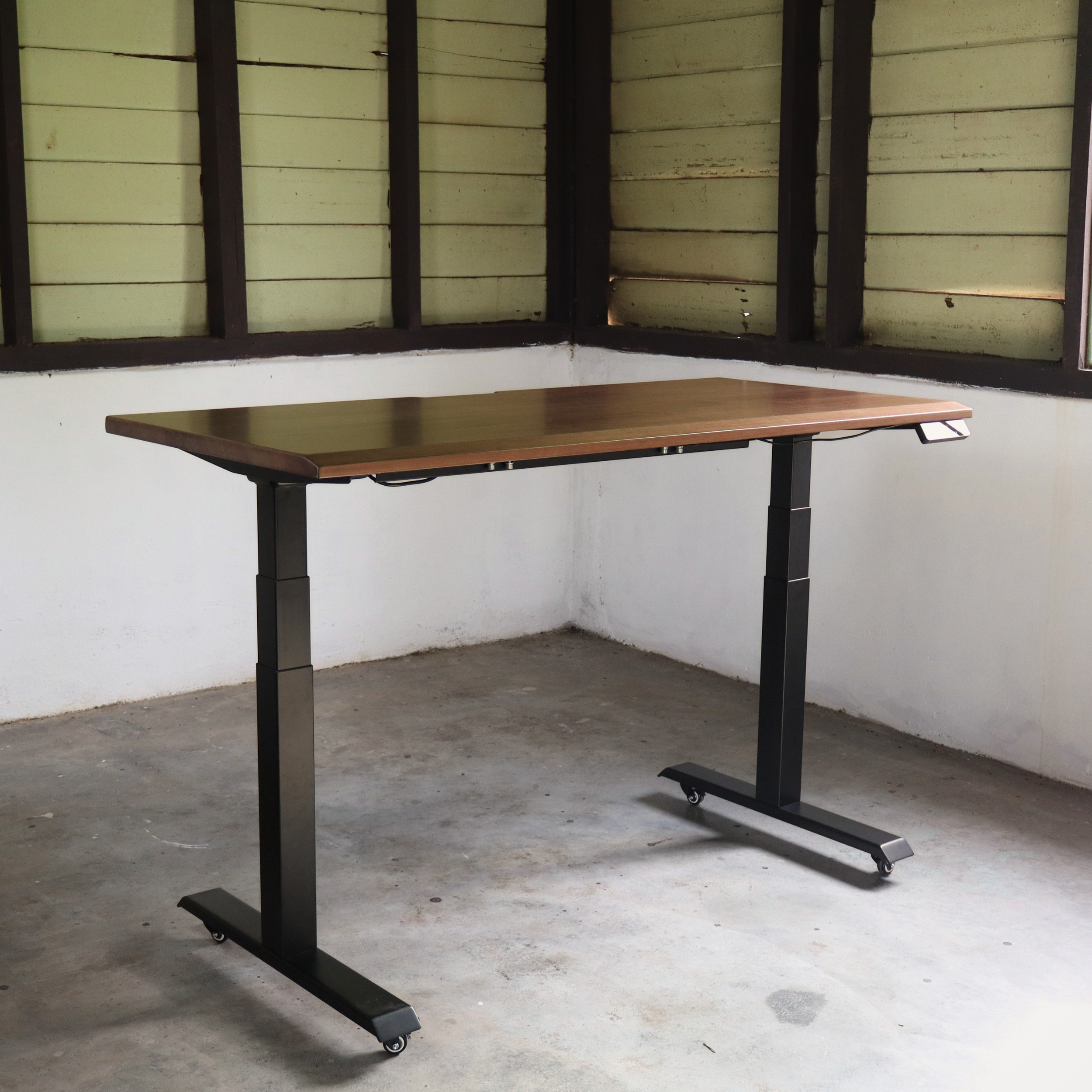 Wooden standing desk with black metal frame in a room with windows and concrete floor.