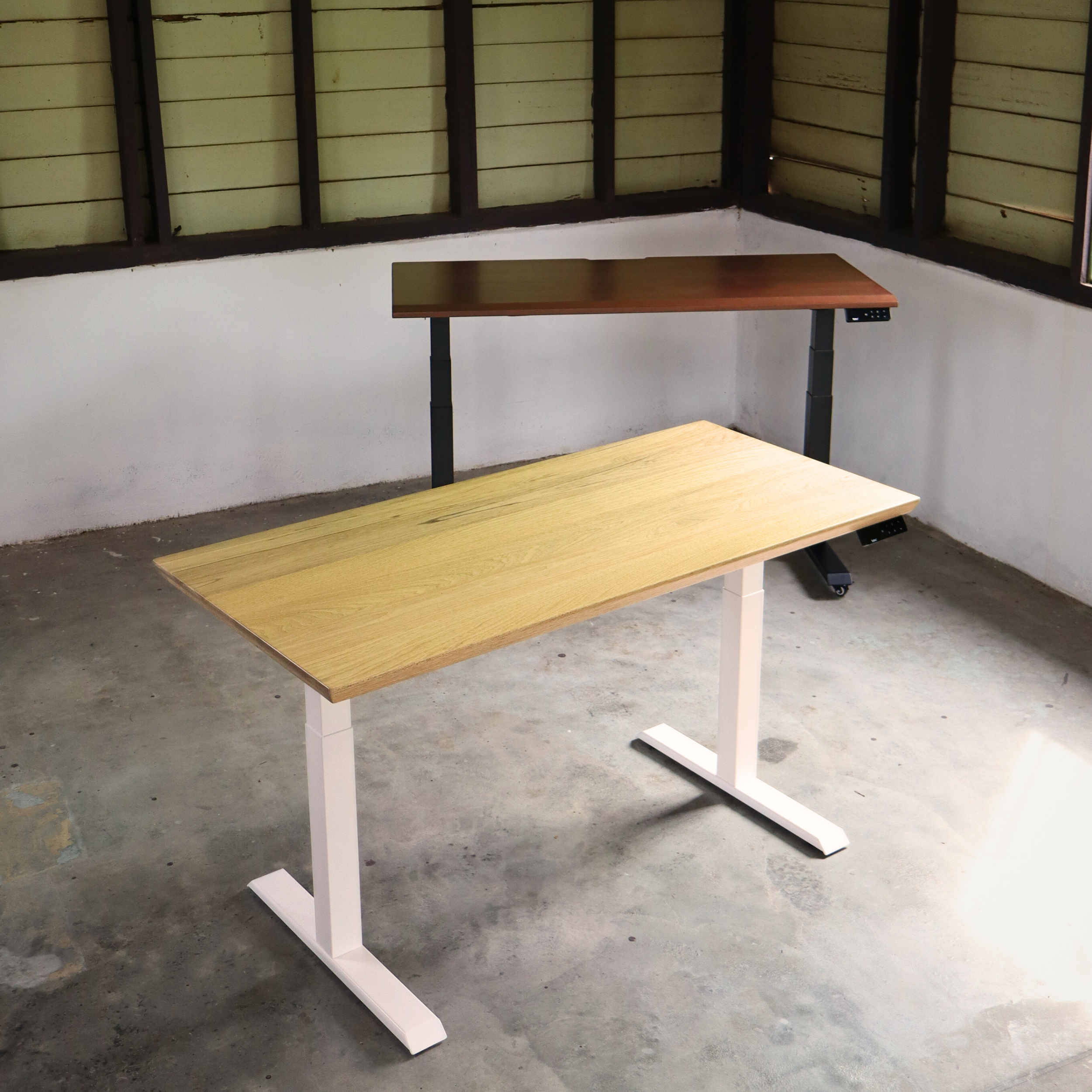 Two adjustable height desks in a room with concrete floor and wooden panel walls.