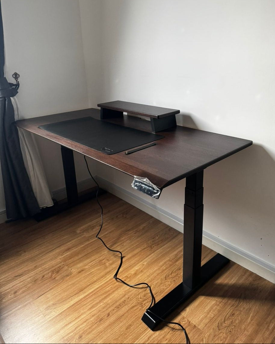 Wooden standing desk with black legs in a room with wooden flooring and white walls.
