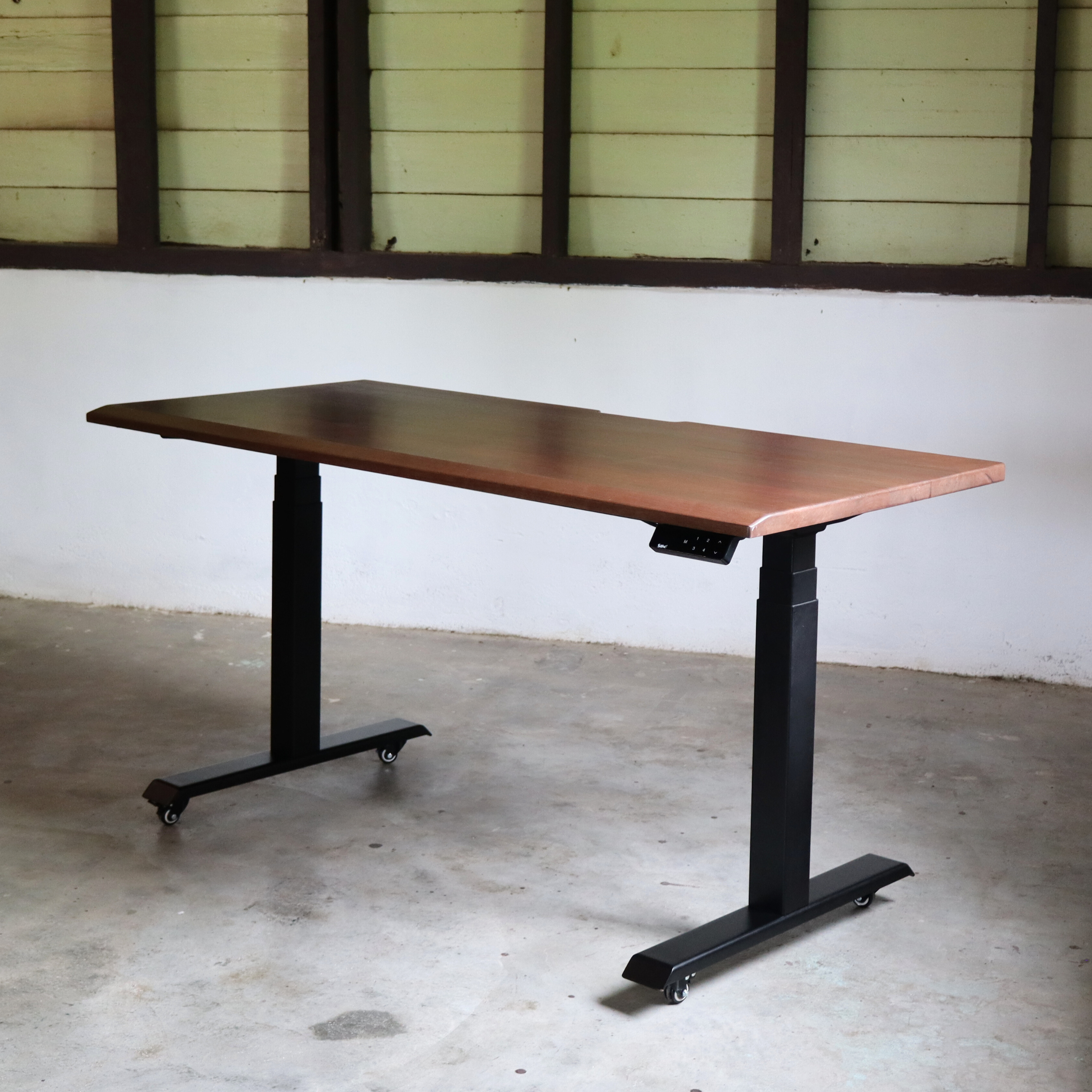 Wooden standing desk with black adjustable legs in a room with white walls and a concrete floor.
