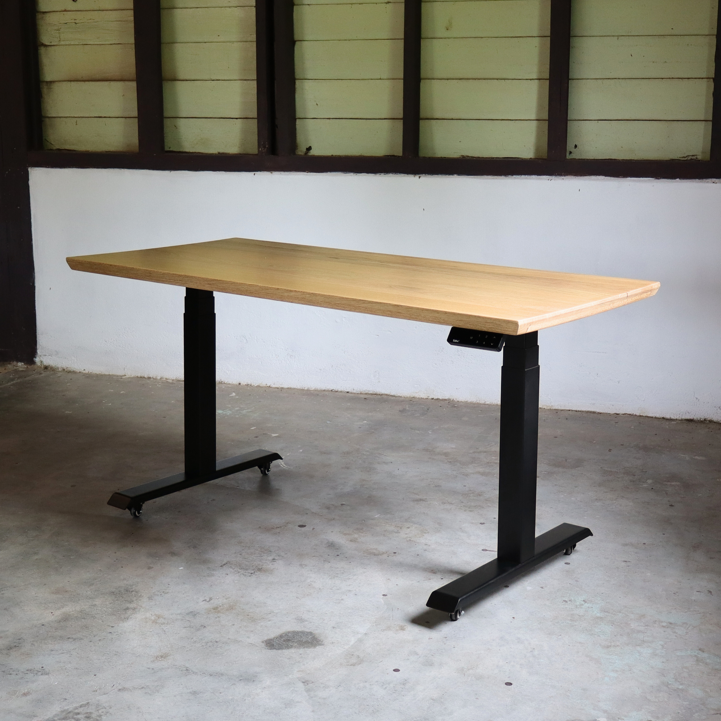 Wooden Standing desk with black metal legs in a room with concrete floor and wooden walls.