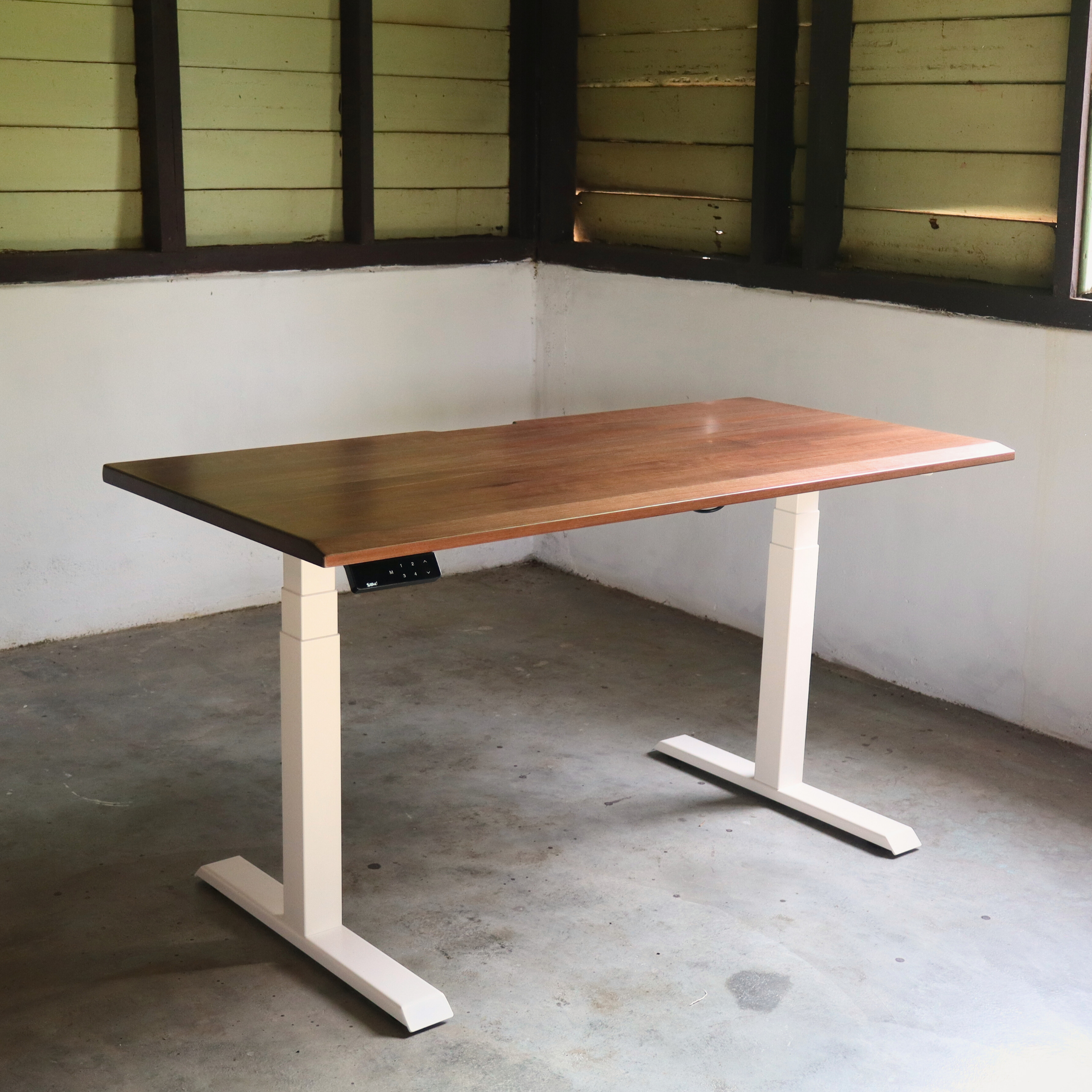 Wooden standing desk with white legs in a room with concrete floor and wooden walls.