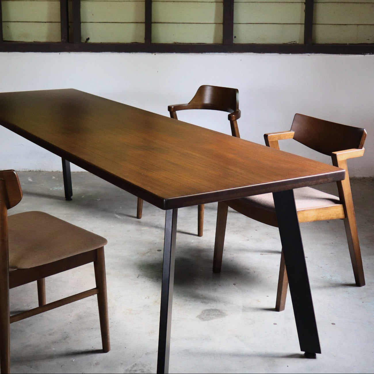 Wooden dining table with chairs in a room with a white wall and wooden paneling.
